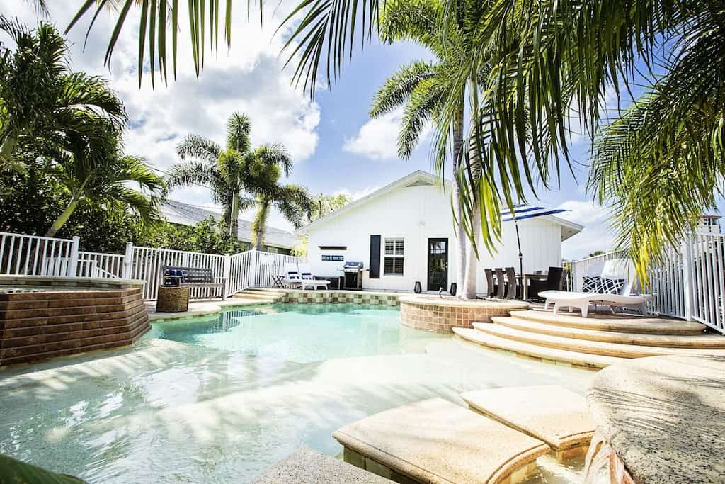 View of the pool, palm trees, and the back of the whitewashed Vanderbilt cabin, one of the best Airbnbs in Naples. 
