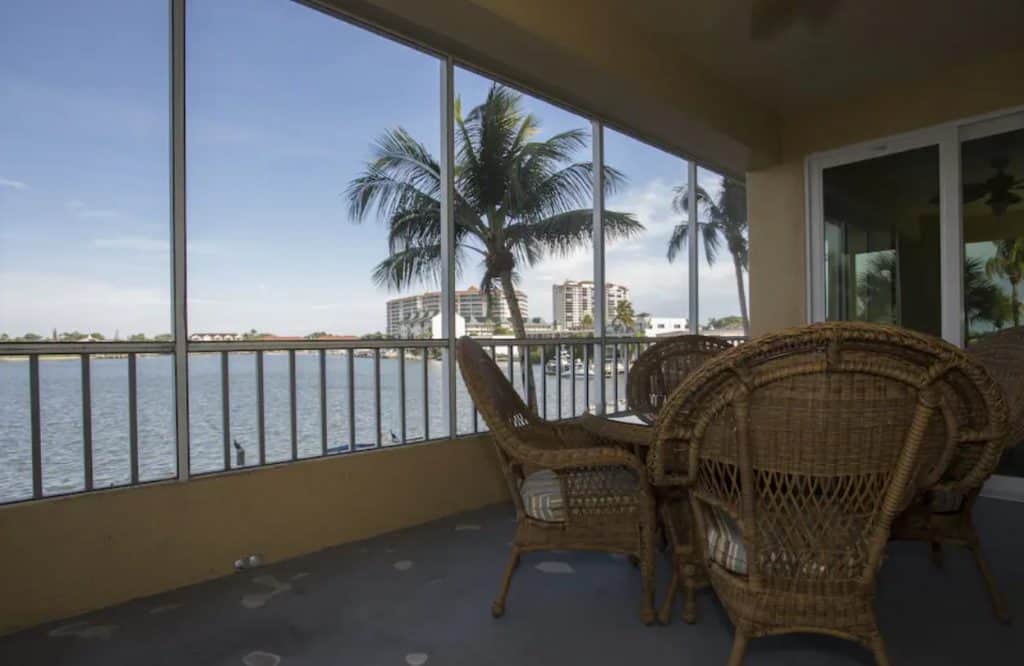 The private balcony that overlooks the Gulf of Mexico at a resort in Naples FL. There is a set of whicker furniture and the balcony is screened in. You can see the coastline and palm trees.