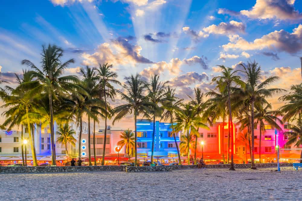 Sunset over the palm trees and colorful, brightly lit buildings of Miami Beach.