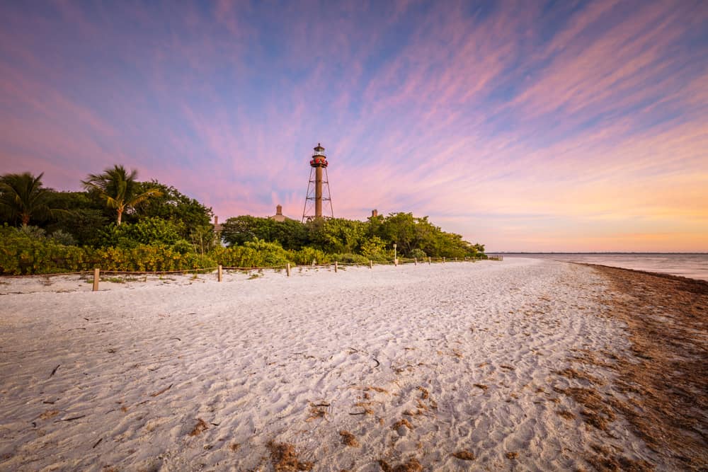 Sunset over one of the beaches of Sanibel Island with beautiful sand and the lighthouse in the distance.