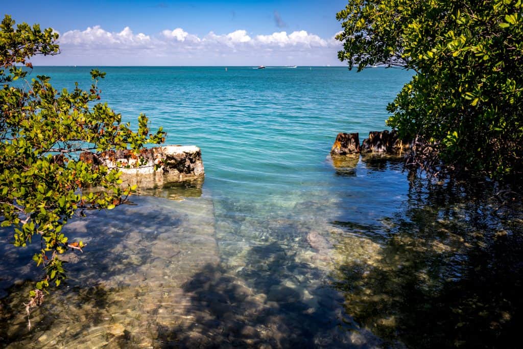 A picture looking directly at an entrance to a swimming area in Biscayne bay just past the shore. The water is clear and you can see the brown rocks at the bottom, it's one of the best places to visit in Miami