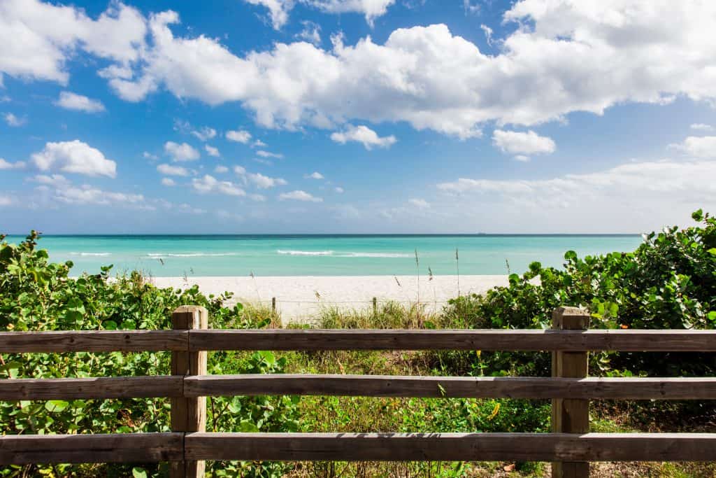 A view of surfside beach, one of the best places to visit in Miami, from the trail with a wooden fence in the foreground