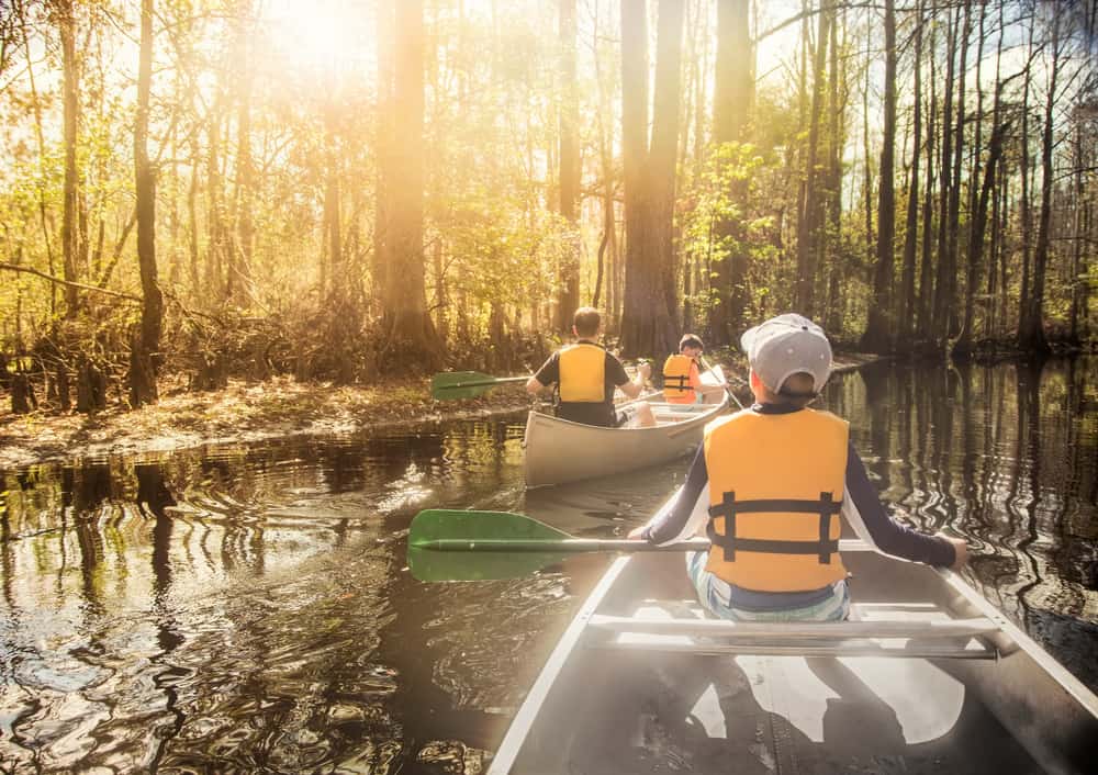 Family canoeing down a river among trees wearing life jackets and items from their Florida packing list.