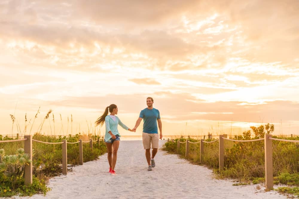 Couple walking hand in hand near a beach in Florida at sunset.