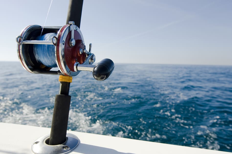 A fishing rod on the edge of a boat looking over blue water.