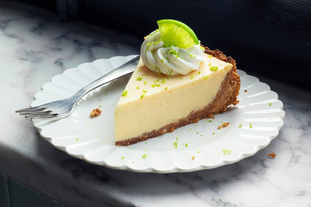 A slice of key lime pie and a fork on a white plate.