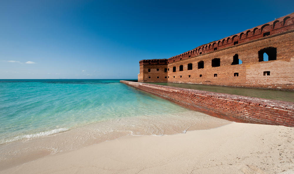 A section of the brick structure of the old Port Jefferson stretches from the beach into blue water and blue sky at the Dry Tortugas National Park.