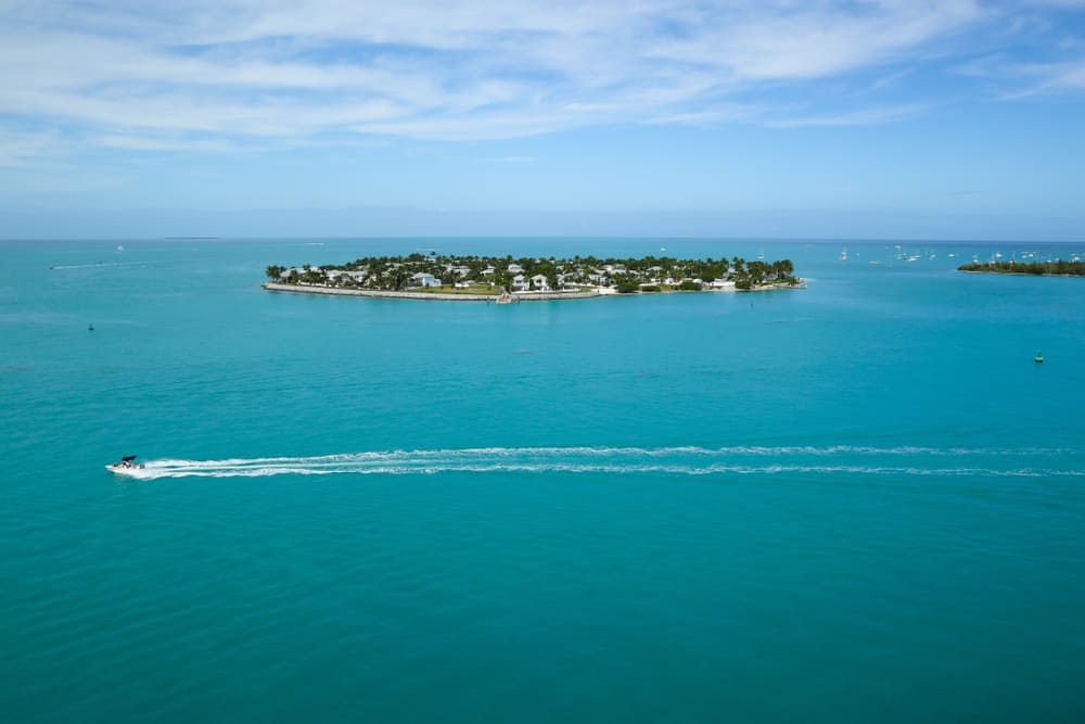 A speedboat cuts through turquoise water and passes the small island of Sunset Key, which has one of the best beaches near Key West.