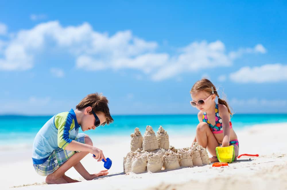 A girl and boy on a beach building a sandcastle with clothes from a Florida packing list.