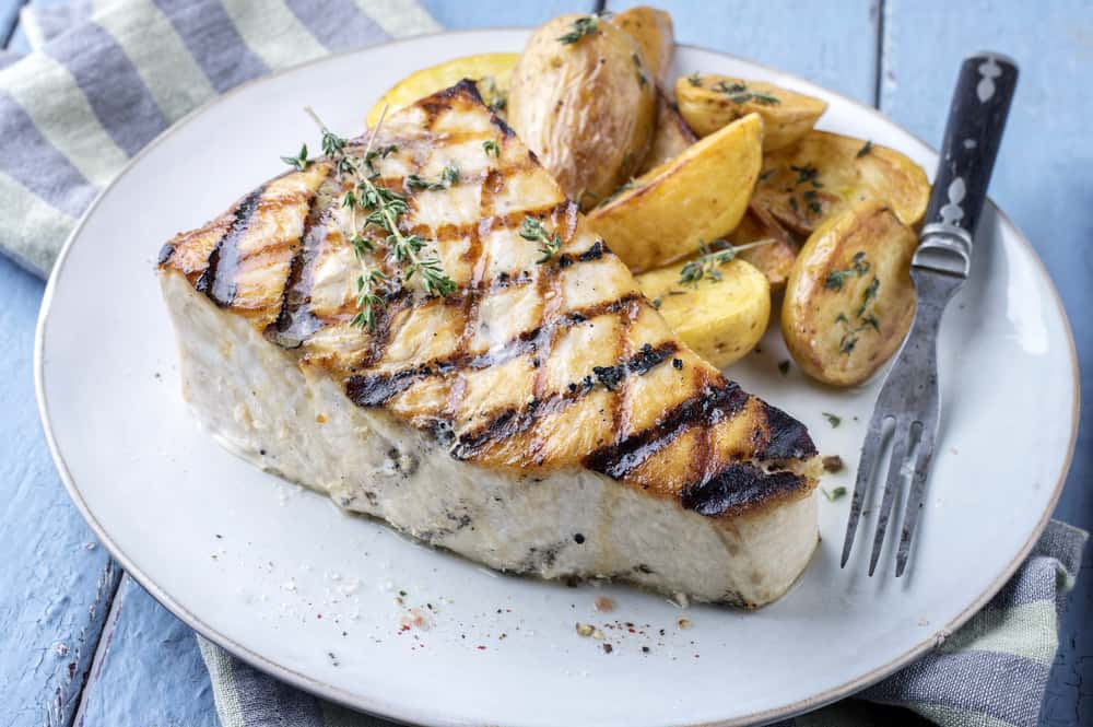 A plate of grilled swordfish with potato wedges on the side.