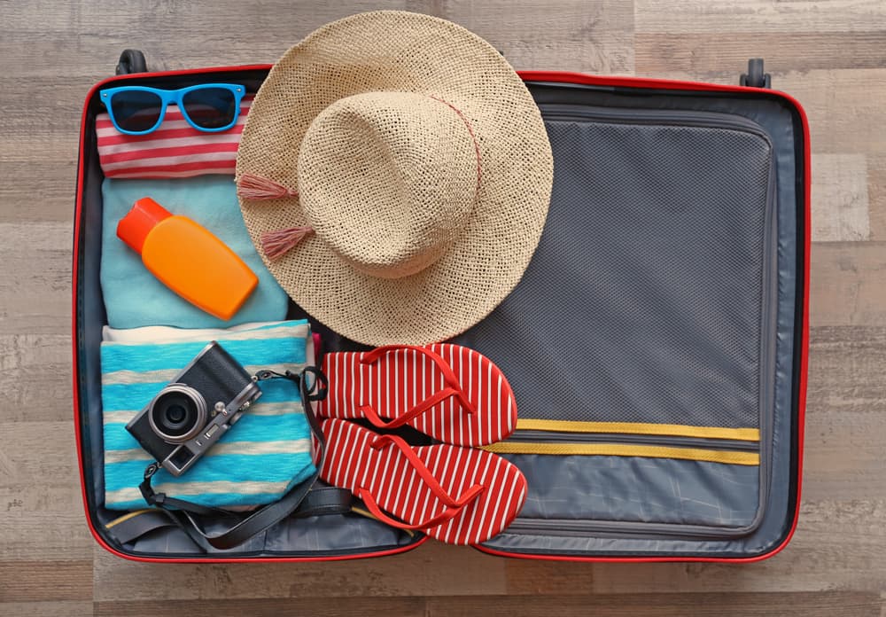 Open suitcase with a floppy hat, flip-flops, camera, and other Miami packing essentials.