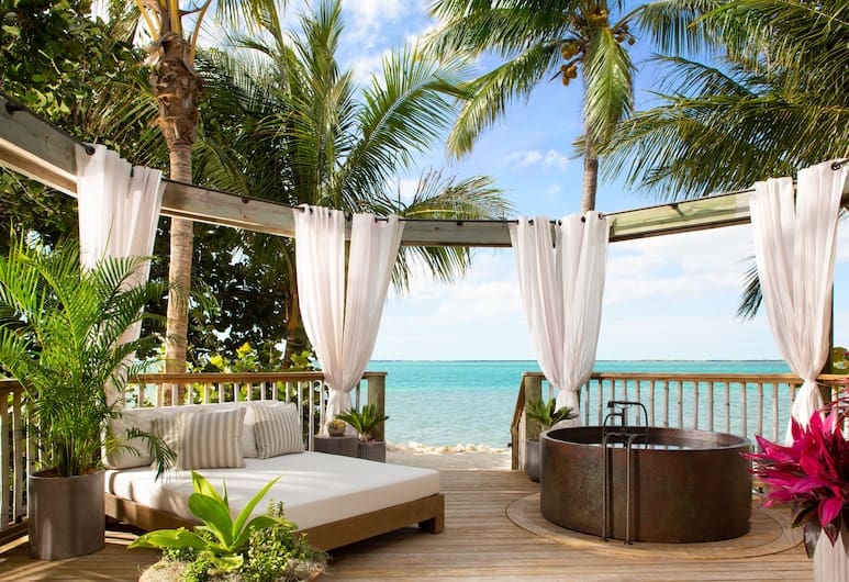 A day bed and metal tub sit on a beachside platform, surrounded by plants and curtains, at an all-inclusive resort in Florida, which makes for a luxurious option for romantic getaways in Florida.