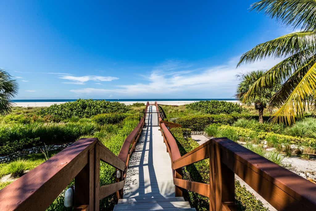 A vegetation and palm tree-lined boardwalk leading to a white sand beach on Marco Island, one of the best romantic getaways in Florida.