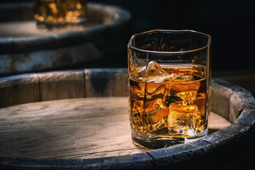 Glass of iced rum on top of a barrel.