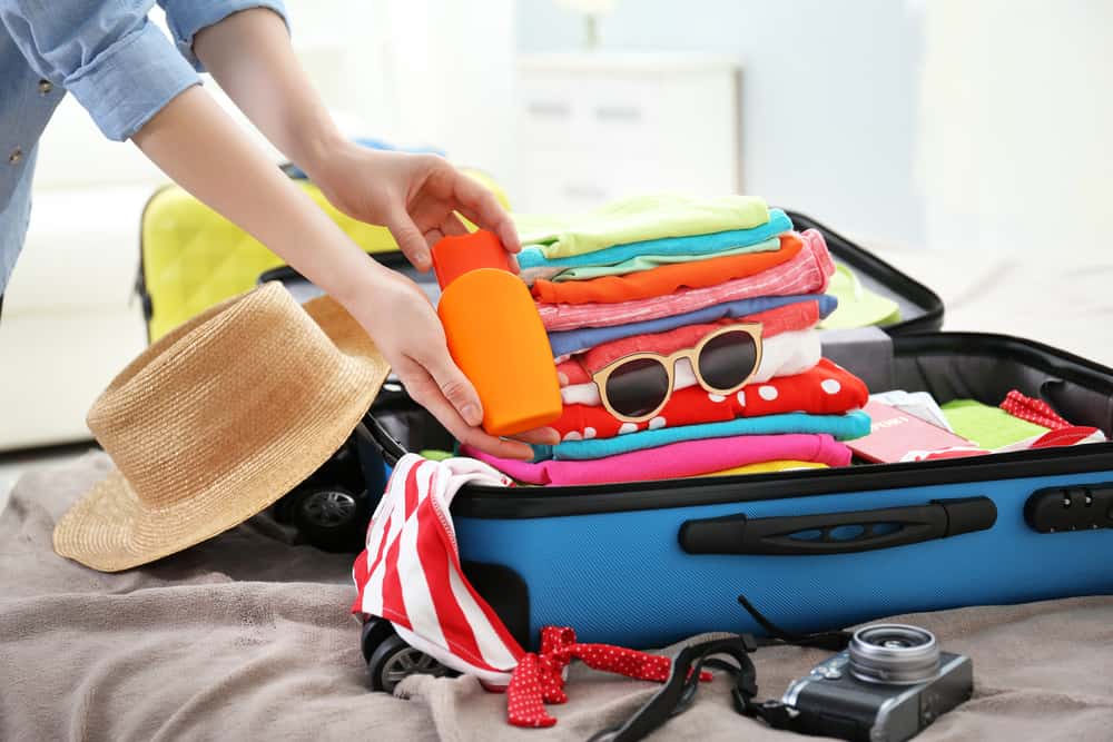 Woman packing a bottle in a full suitcase of clothes.