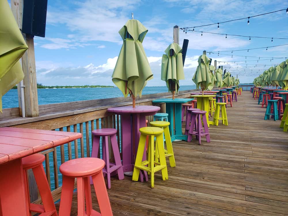 Colorful stools and tables with collapsed umbrellas lining Sunset Pier with string lights overhead during the day.