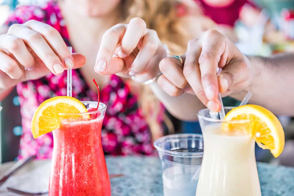 Two people's hands dip straws into two alcoholic drinks, one a strawberry daiquiri and one a pina colada, as they sit outside at a restaurant like Snook Inn in Marco Island.