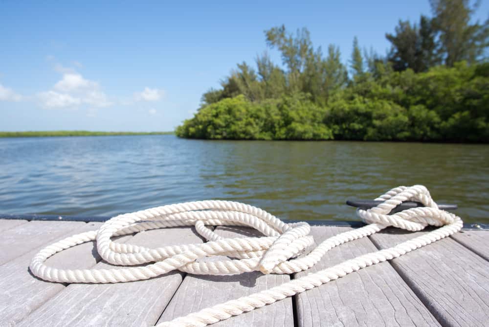 A piece of rope sits tied to a boat dock in Vero Beach FL, with water and green vegetation in the background, where fishing is one of the best things to do in Vero Beach.