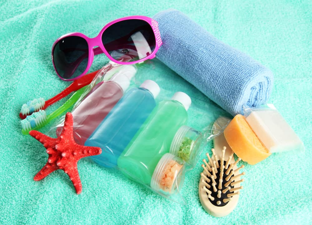 A selection of toiletries, a pair of sunglasses, and a rolled towel on a green towel background.