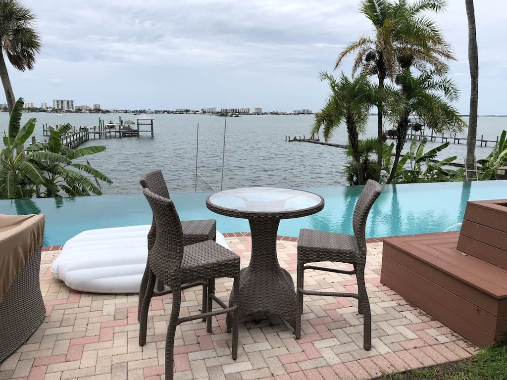 View of the porch, infinity pool, and bay beyond of this waterfront home property. 