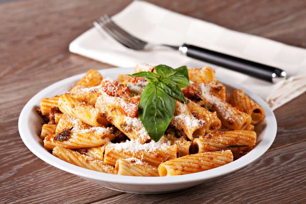 Bowl of beef bolognes rigatoni with fork and napkin.
