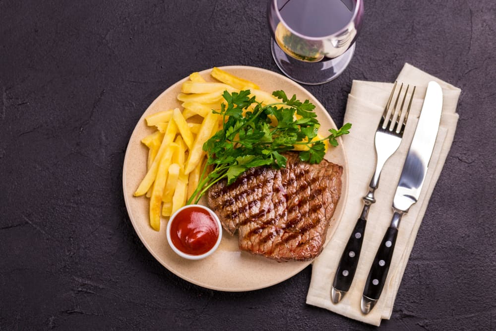 A plate of steak frites with knife and fork on a black background.