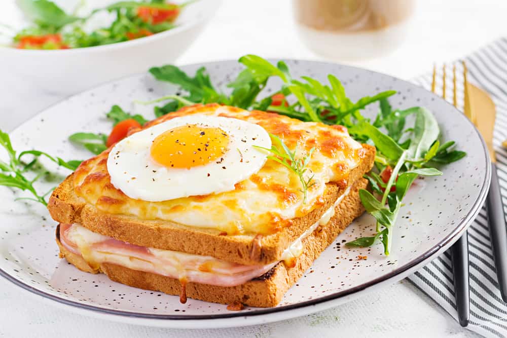 A Croque madame sandwich with a fried egg on top and a side salad.