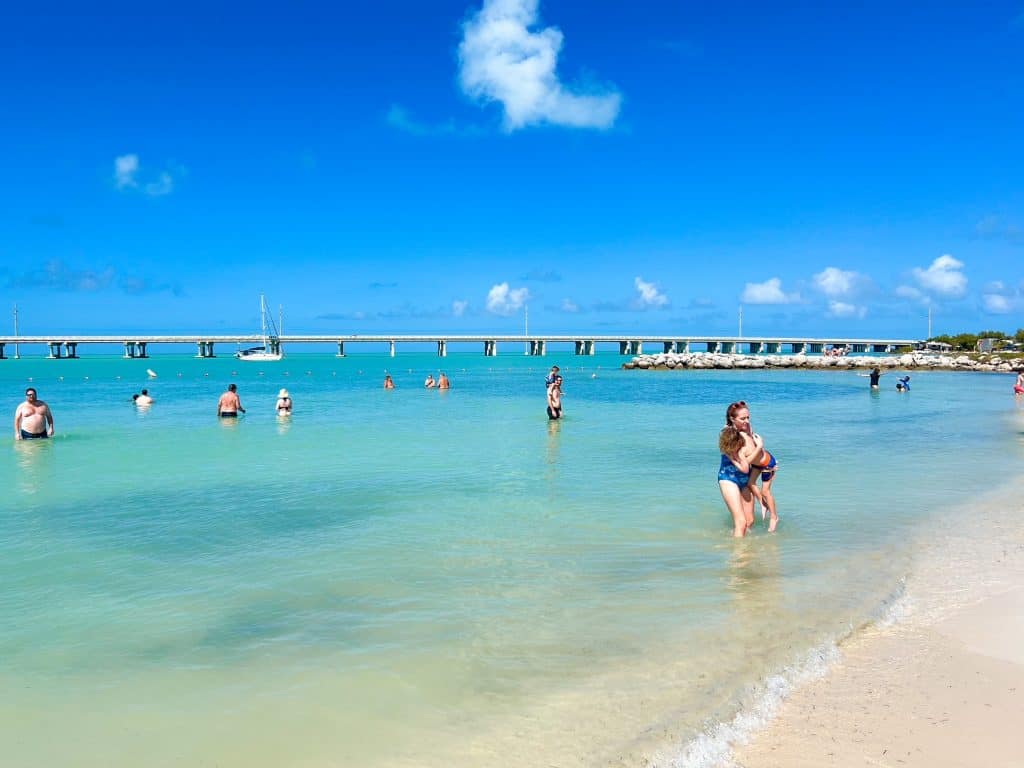 Families and friends play in the blue waters of Bahia Honda State Park with the new bridge in the distance.