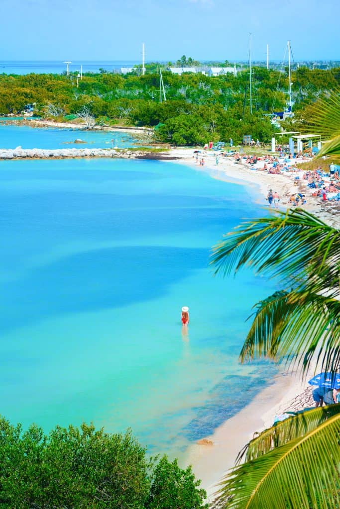 An ariel shot of a woman in a red bathing suit and sun hat, wading through the water at Bahia Honda State Park.