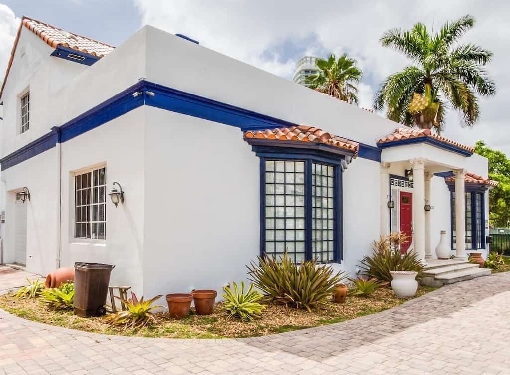 Outside view of the Jewel of South Beach, house has bay windows, white stucco siding, blue trim, and a red terracotta tile roof. 