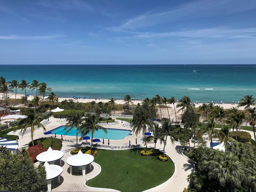 View of a covered picnic area, palm trees, pool, and turquoise ocean from the Sea View Condo. 