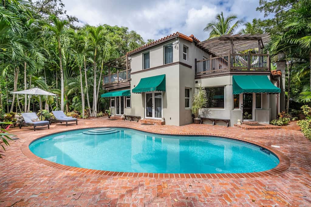 View of the pool and back side of the Secret Garden house. The house is two stories with a really cool covered deck and hammock visible on the second floor. It is surrounded by a lush forest. 