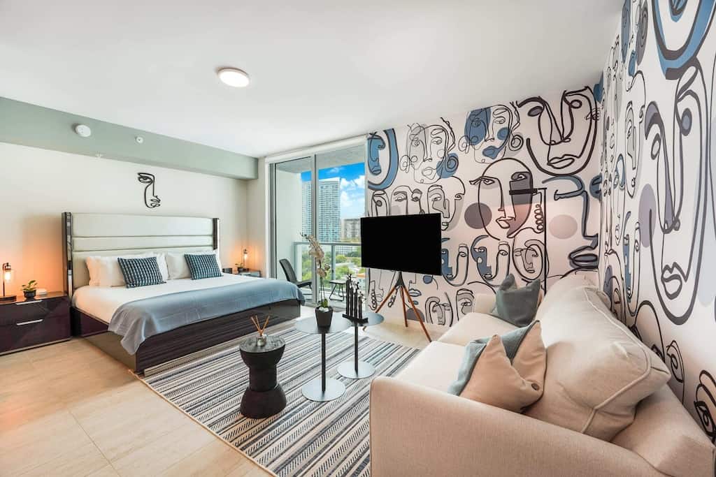 View of the couch and bed of the Artsy Studio apartment, with its groovy blue and grey abstract faces wallpaper