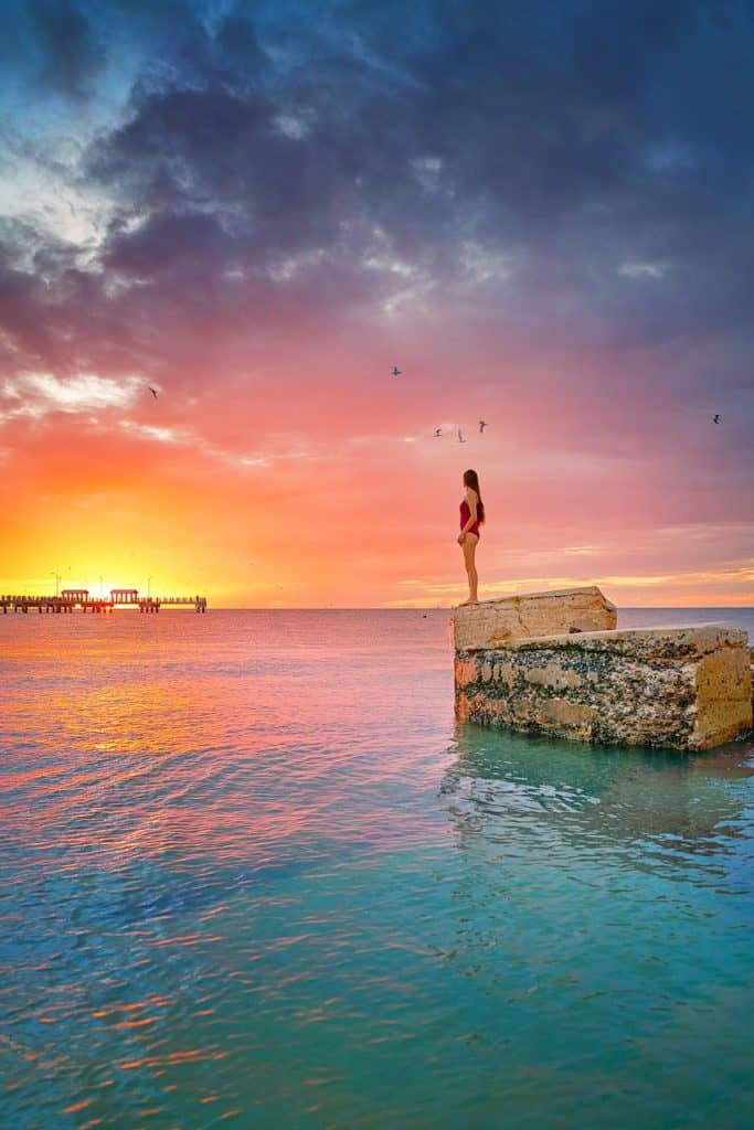 A girl in Red swimsuit standing on abandoned ruins in the ocean at sunset time