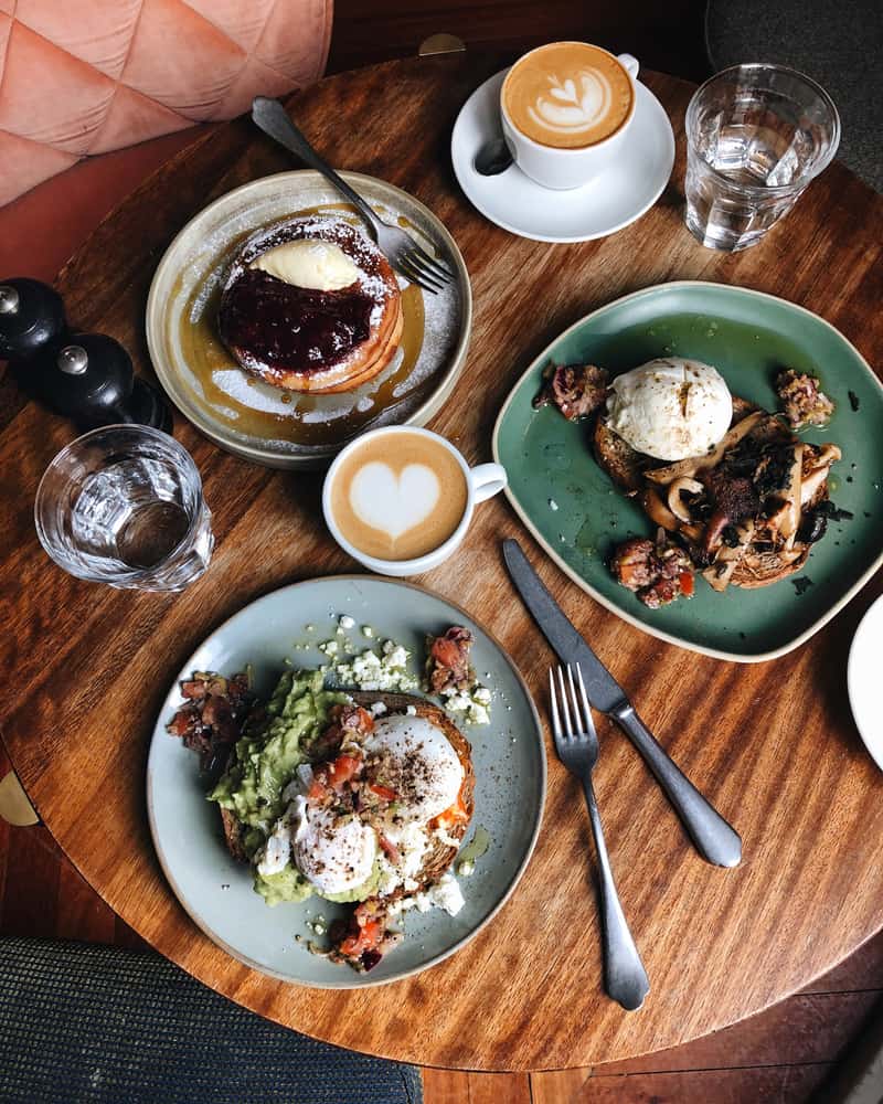 Try a delicious brunch with coffee, pancakes, omelette, and avocado toast with egg on a large wooden table