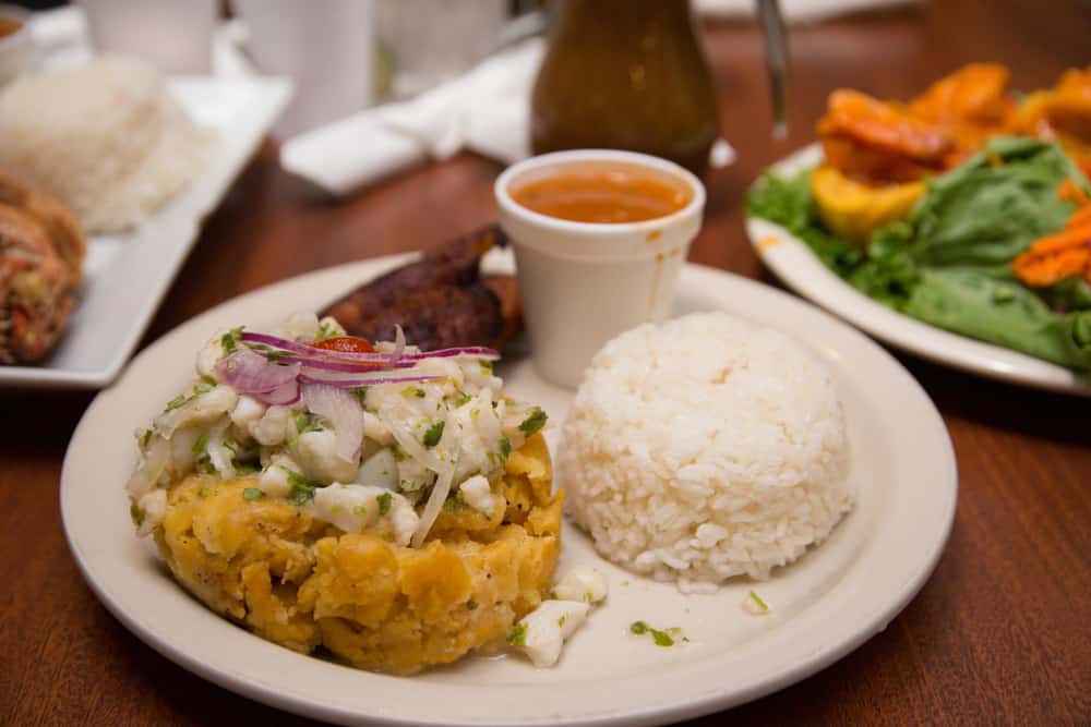 A plate of Latin food with white rice, fried plantains and momofongo topped with ceviche 