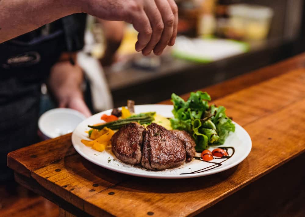 A steak with salad and veggies on a plate on a wooden table