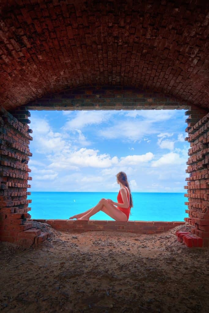 a girl in red swimsuit sitting inside one the brick window cutouts at Fort Jefferson overlooking the ocean 