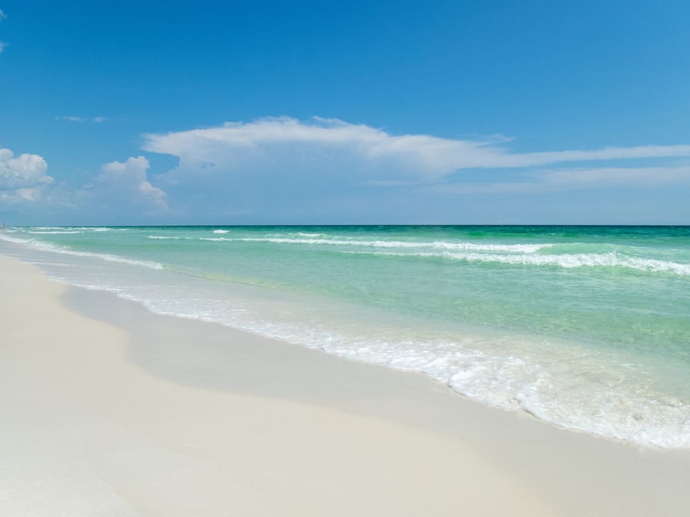 Emerald green water washes up in waves on the sand of Henderson Beach State Park, one of the best Panhandle beaches in FL.