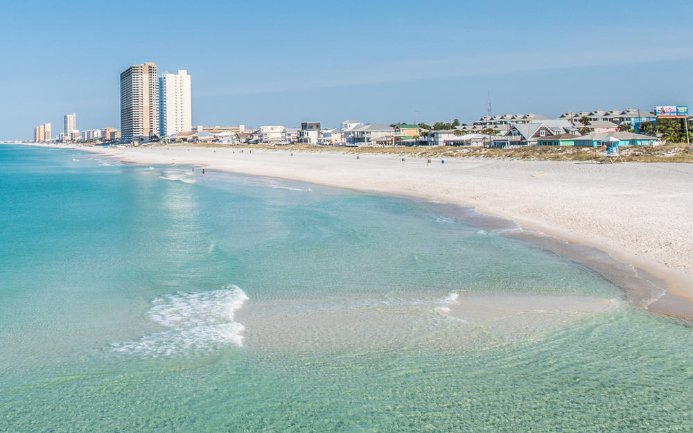 High rise buildings and beach cottages line the shore looking out on light blue water along Panama City Beach, one of the best Panhandle beaches.