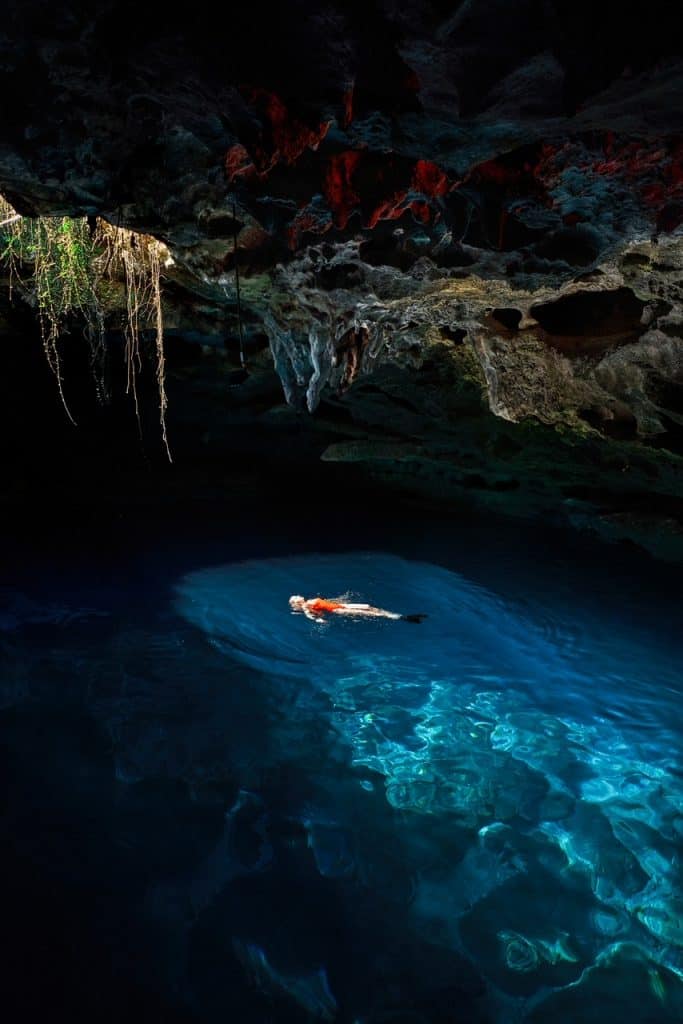 A woman in a red bathing suit floats on her back in the enclosed area of Devil's Den.