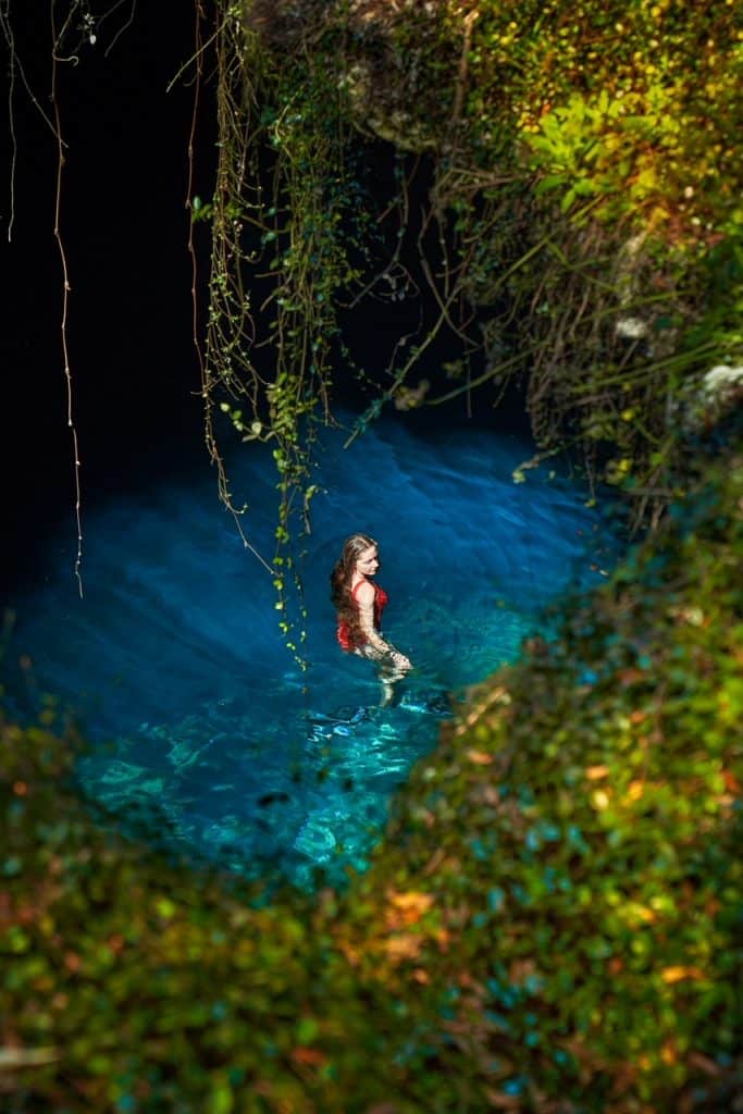 From the chimney top perspective, a woman is seen swimming below the hole in the ground, in the blue water of Devil's Den.
