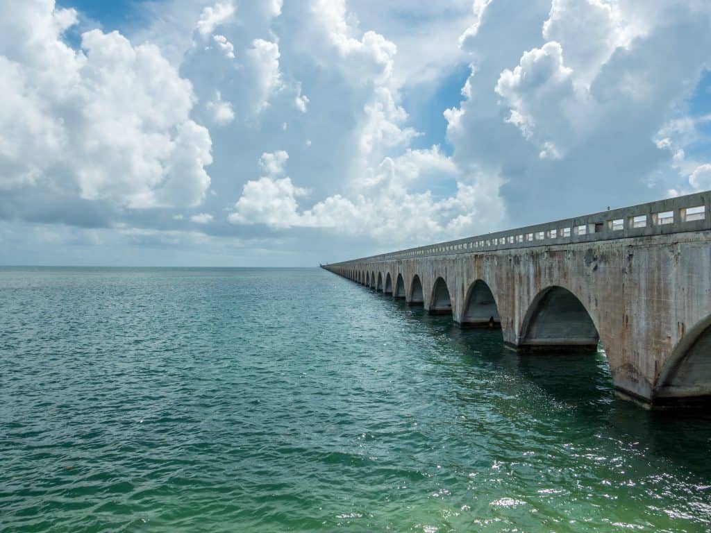 A picture of the the old 7-mile bridge, the grey concrete of the bridge is dappled with dark brown rust, making a beautiful contrast against the emerald waters it stands on 