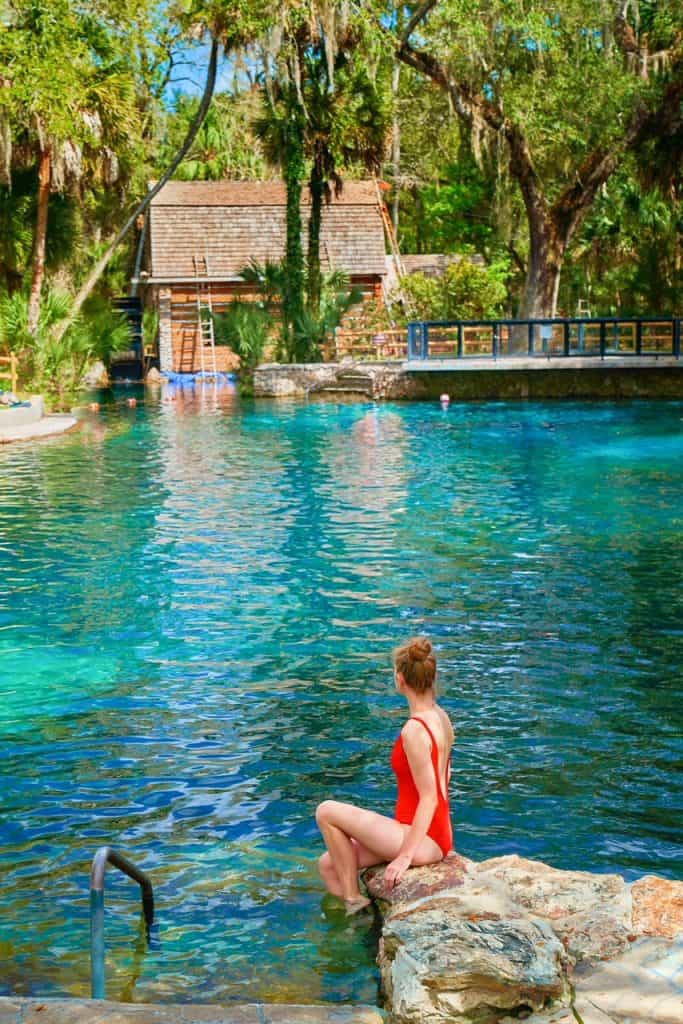 A woman in a red bathing suit perches on the edge of the wall that surrounds the spring at Juniper Springs.