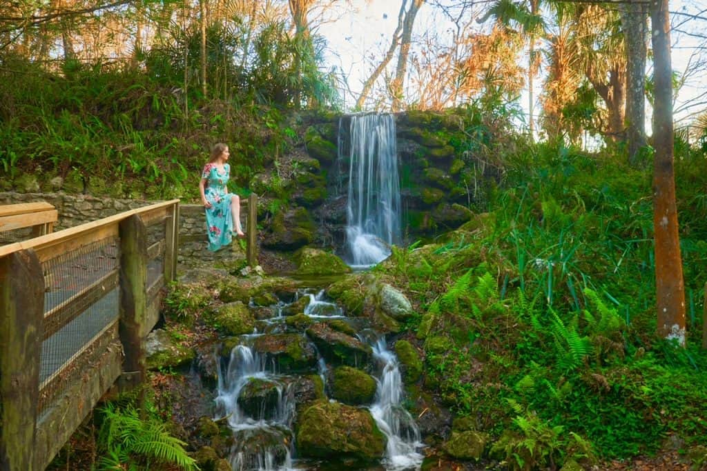 A woman in a floral dress perches on the wooden banister of the walkway that comes from the trail that leads to the man-made waterfalls at Rainbow Springs.