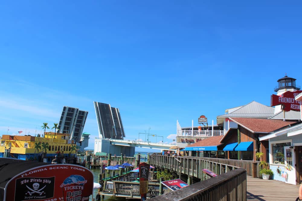 The wooden boardwalk at John's pass village with the bridge open in the background and restaurants along the boardwalk