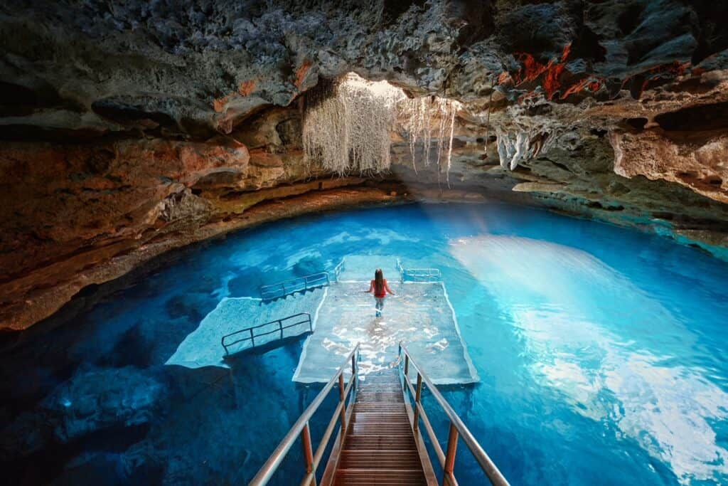 A girl stands on a platform in the blue water in the underground Devil's Den.