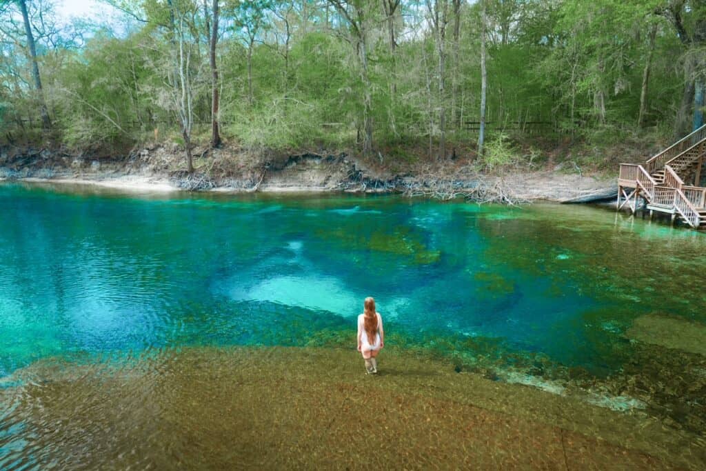 A woman in a white swim suit stands in the multi-colored water of Little River Springs.