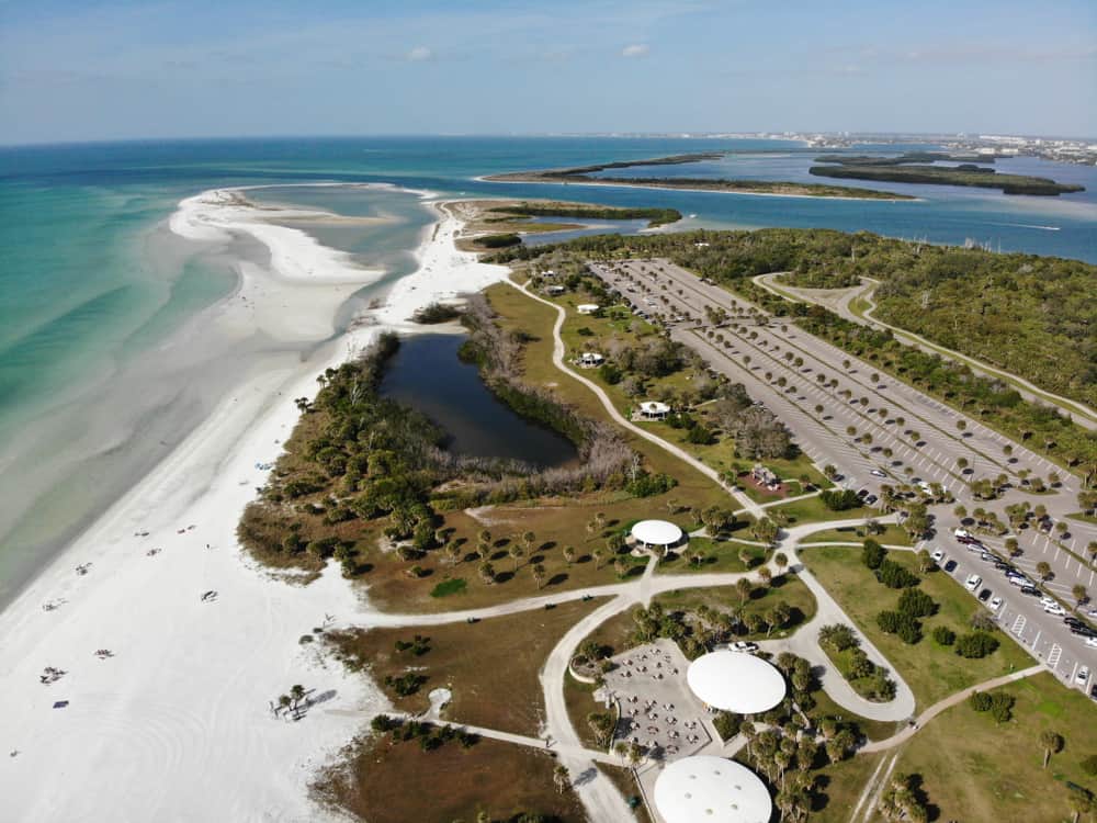 An aerial view of Fort Desoto Park, with white sand beaches, a parking lot, and palm trees dotted throughout.