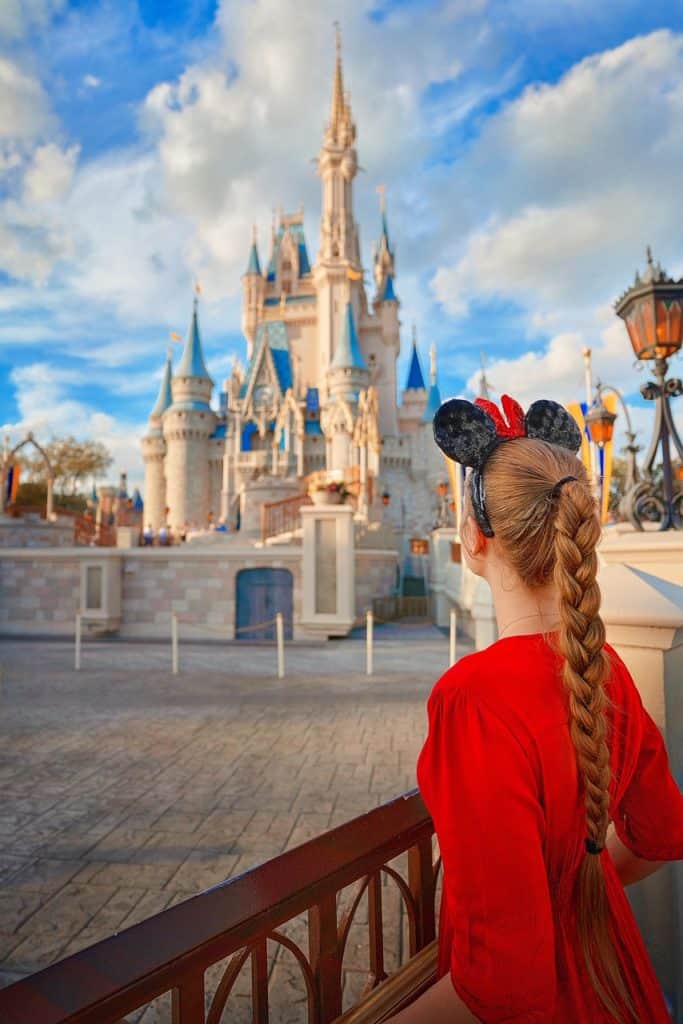 A woman in a red dress with a mouse ear headband looks out on the castle at Walt Disney World, one of the most popular weekend getaways in Florida.